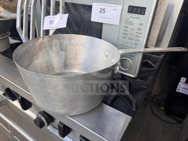Aluminum sauce pan with long handle, used condition, placed on a stovetop. Visible auction labels, no brand marks.