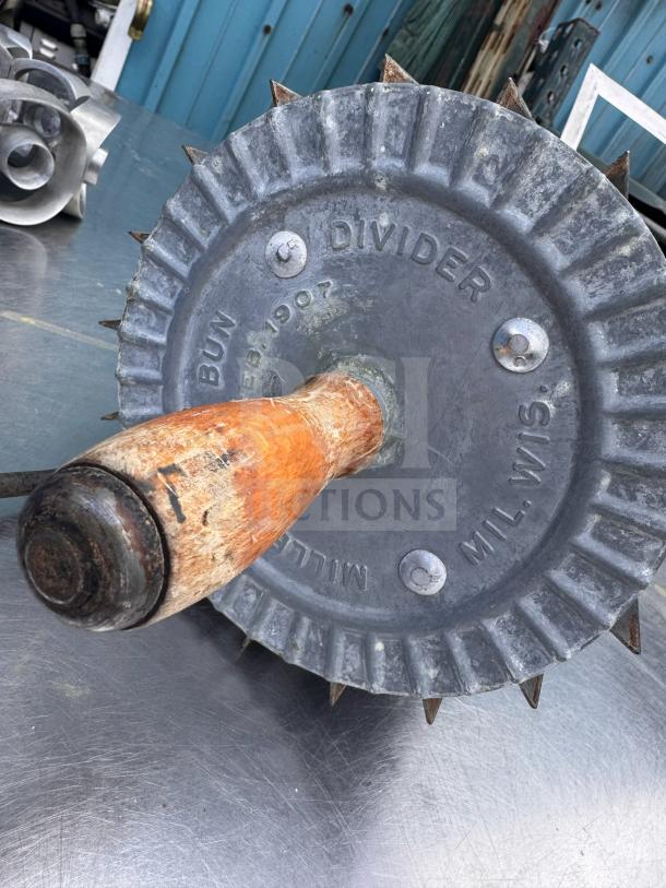 Vintage Miller bun divider with spiked metal wheel and wooden handle, marked "MILLER MIL.W DIVIDER" in used condition.