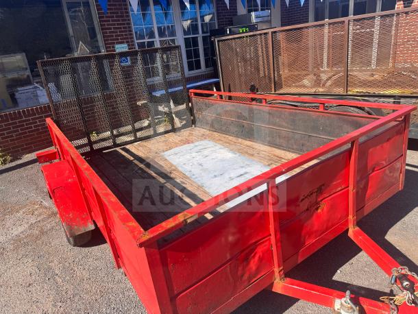 Red utility trailer with metal mesh gate, wooden floor, and visible wear. No title. Perfect for hauling and transport needs.