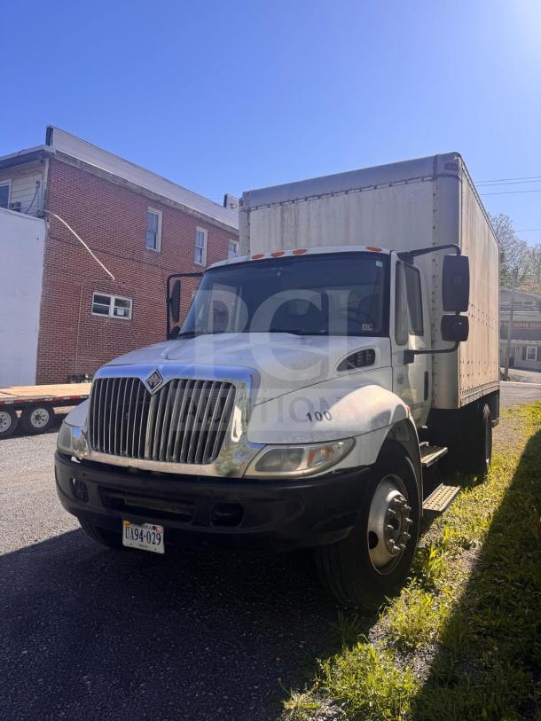 White box truck parked on gravel, showing wear. Features a large cargo area, dual rear wheels, and visible license plate.