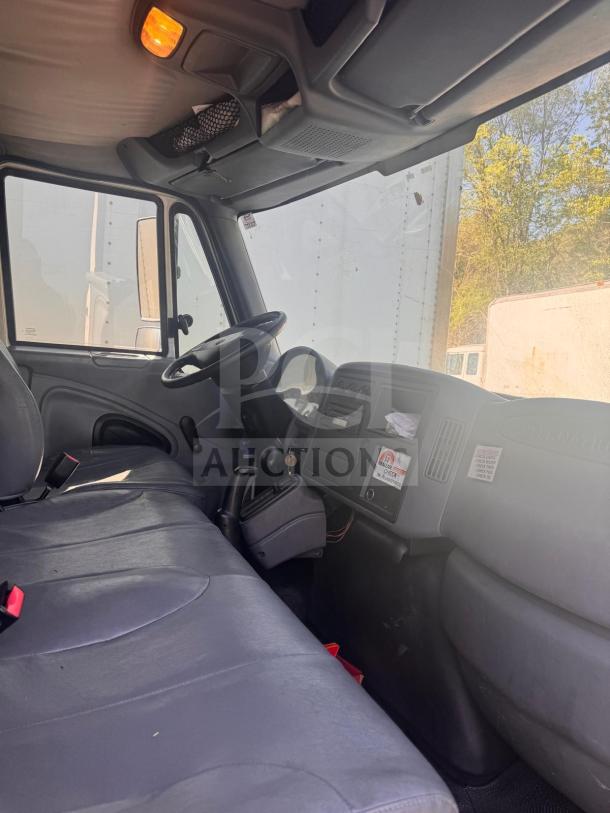 Interior of a box truck showing gray fabric seats, steering wheel, and dashboard with operational controls, in used condition.