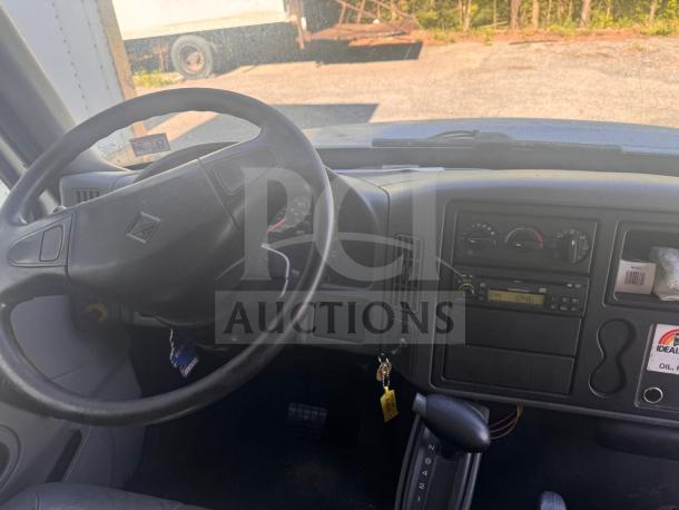 Steering wheel and dashboard of box truck; features include radio, temperature controls, and ignition with keys.