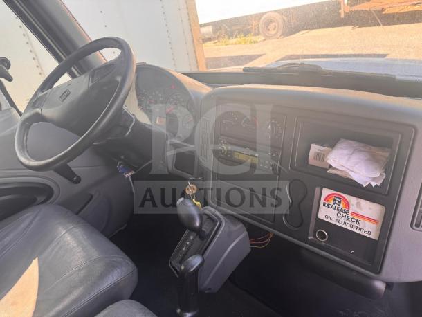 Interior view of a box truck cab showing steering wheel, dashboard with dials, and Idealease label indicating maintenance checks.