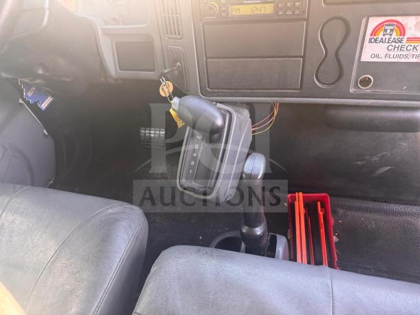 Box truck interior, featuring a black gear shift, gray upholstery, and IDEALLEASE maintenance checklist label. Dashboard visible.