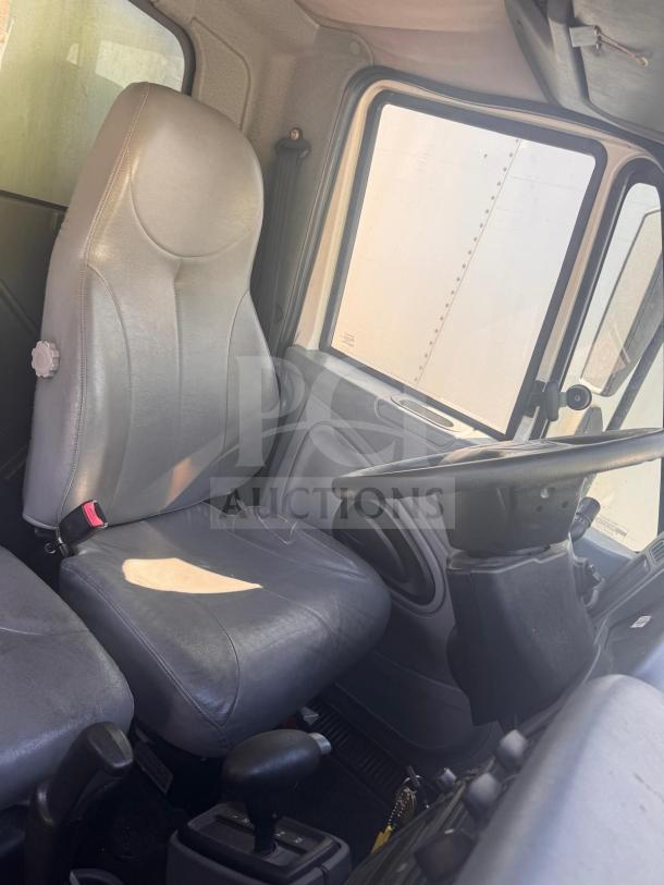 Interior of a box truck cabin with a gray leather driver's seat, steering wheel, and visible control dashboard.