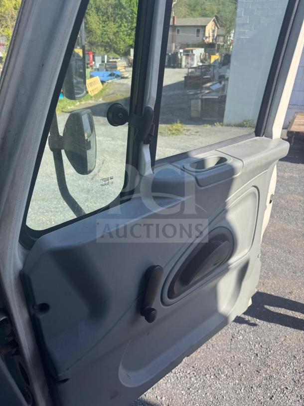 Interior view of a box truck driver's side door. Manual window crank, light gray paneling, and exterior side mirror visible.