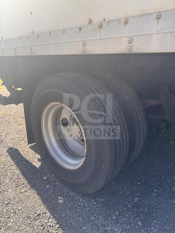 Box truck rear wheel with visible Michelin tire on gravel. Rust spots on truck's side panel. Used condition.