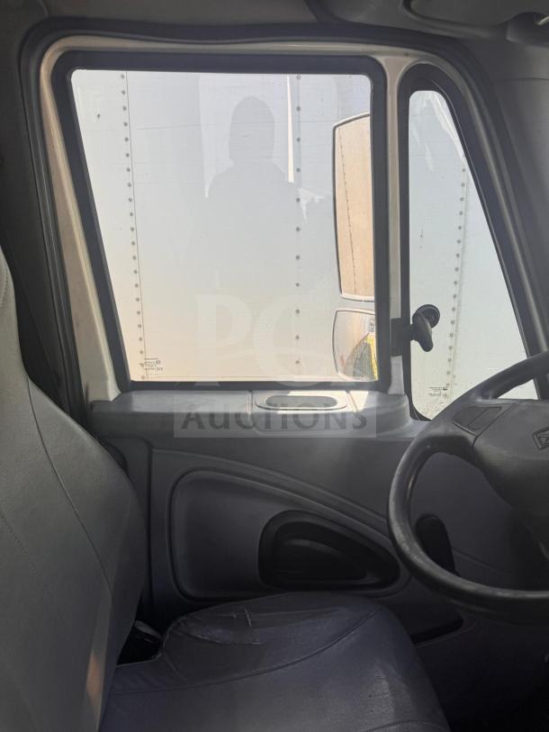 Interior view of a box truck showing the driver seat, dashboard, and window. The seat appears worn, suggesting use.