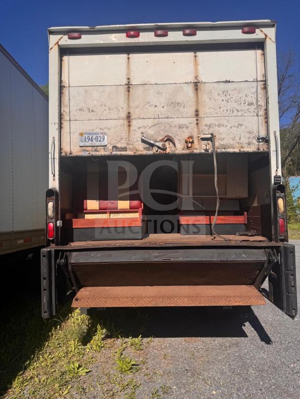 Box truck rear view with open cargo area, visible rust, Virginia license plate UA94-029, and fold-out ramp.