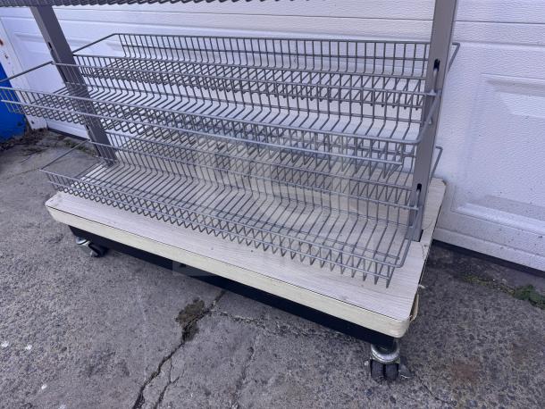 Mobile wire basket shelving unit on wheels, metal frame, four tiers, used condition, ideal for display or storage.
