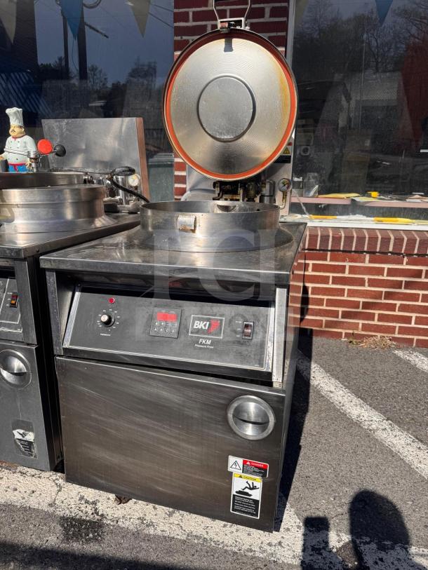 BKI FKM-FC commercial electric pressure fryer, open lid, 208V, stainless steel, warning labels visible, outdoor setting.