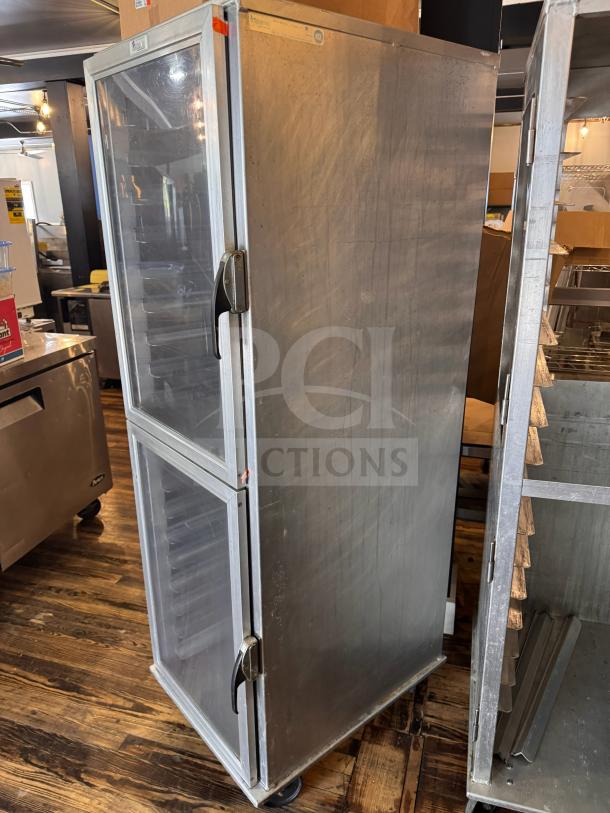 Stainless steel sheet pan cabinet with two clear doors, multiple rack slots, on casters, in good used condition.