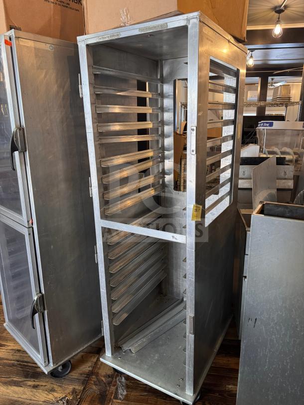 Metal sheet pan rack on casters, open design with multiple slots for holding trays. Features a tag indicating auction lot. Good condition.