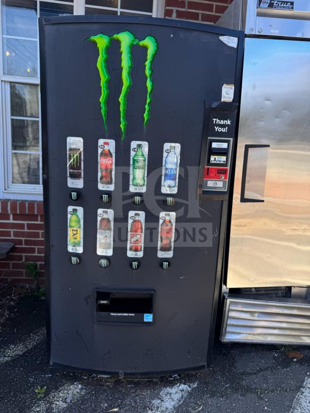 Monster Energy vending machine, black with logos, dispensing various beverages, visible price labels, good condition.