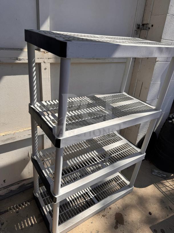 Plastic storage shelving unit with four ventilated shelves, white frame, used condition, suitable for garage or shed organization.