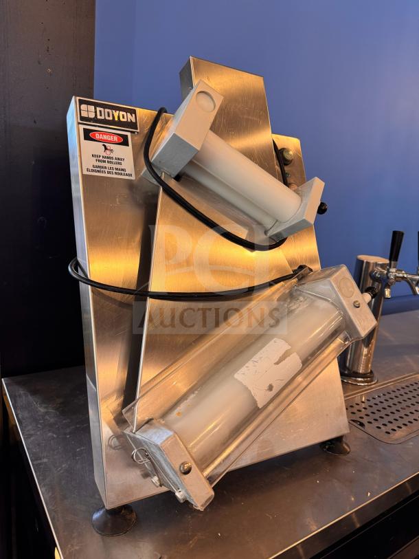 Doyon DL12DP countertop dough sheeter, stainless steel, visible safety label, used condition, compact design.