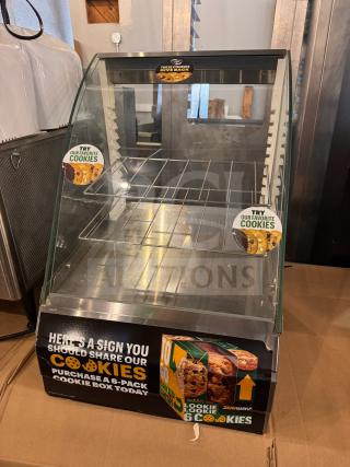 Glass countertop display case for cookies with metal racks. Features promotional cookie labels and a "Purchase a 6-Pack" advertisement.