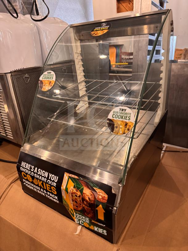Glass and metal display case for cookies, featuring marketing stickers. Good condition with wire shelving and clear panels.