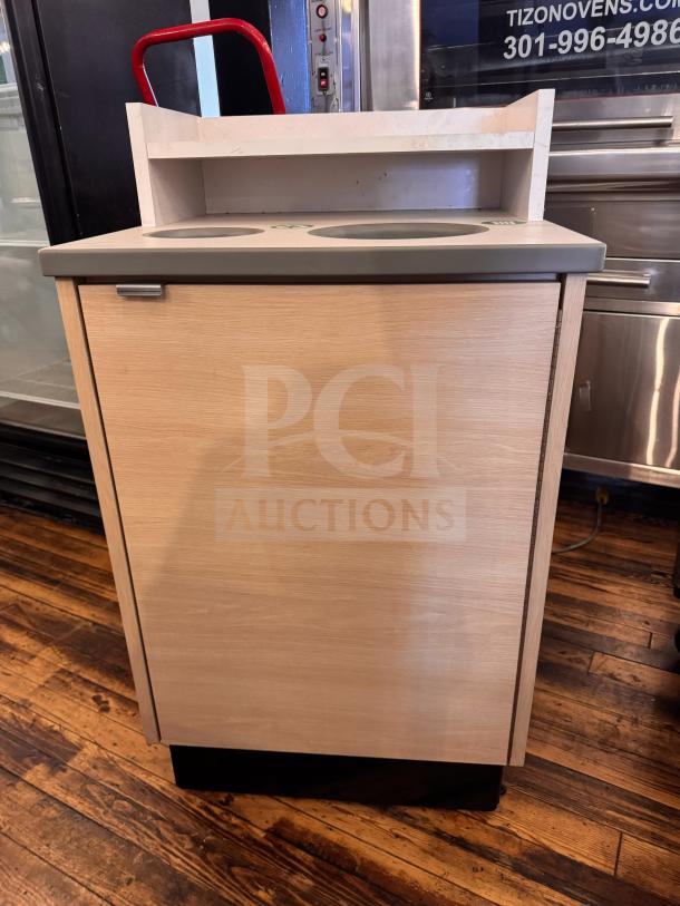 Wooden waste receptacle with dual openings, grey top, and metal handle. Features shelf and smooth finish. Appears well-maintained.