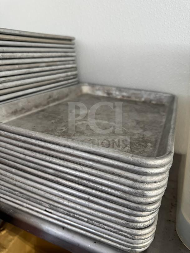 Stack of aluminum baking sheets, showing slight wear, suitable for professional kitchen use.