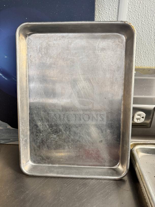 Aluminum baking sheet with visible surface scratches, rectangular shape, good condition, resting on a stainless surface.