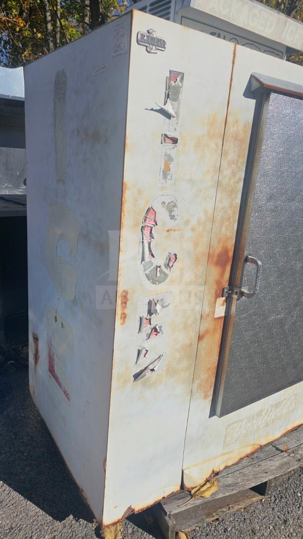 Outdoor upright single solid-door ice merchandiser, worn condition with visible rust and peeling paint, Leer brand.