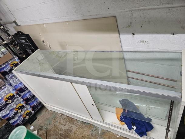 Glass display case with metal frame, sliding doors, and two shelves. Used condition with some wear, suitable for retail display.
