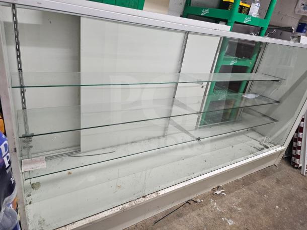 Glass display case with metal frame, featuring three adjustable glass shelves. Visible wear and dust on surfaces.