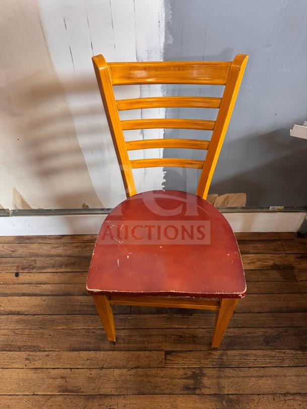 Wooden dining chair with ladder back design and red seat cushion. Shows signs of wear with scratches on the seat.