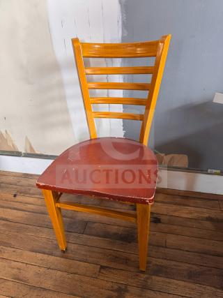 Wooden dining chair with ladder back design, light brown finish, and a red seat showing signs of wear and scratches.