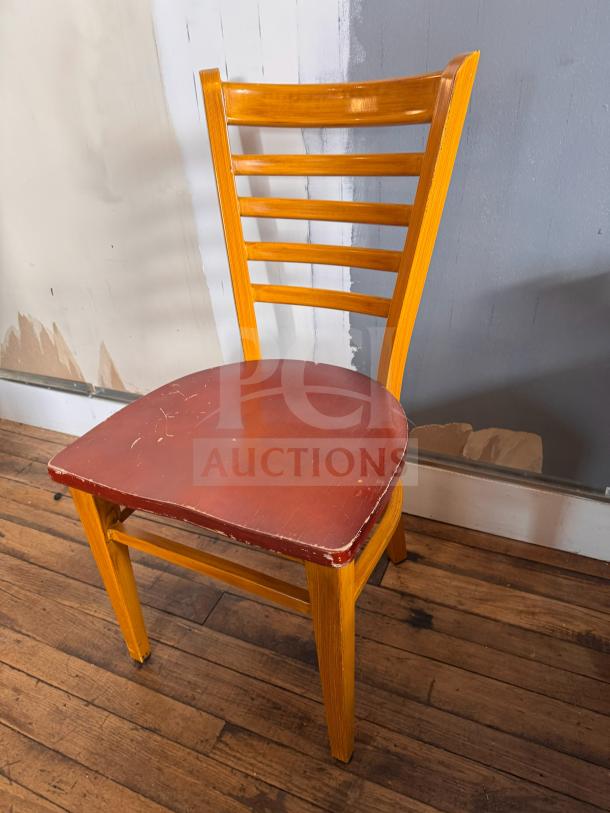 Wooden dining chair with a ladder back design and red seat, showing visible wear and scuffs. Simple and rustic.