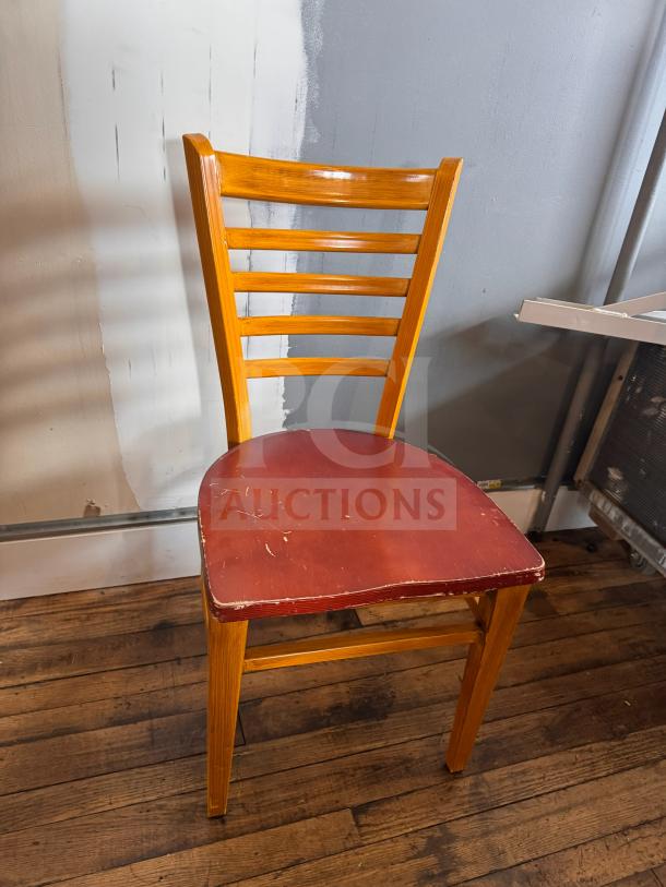 Wooden dining chair with ladder back design, red seat with visible wear, sturdy construction, rustic appearance.