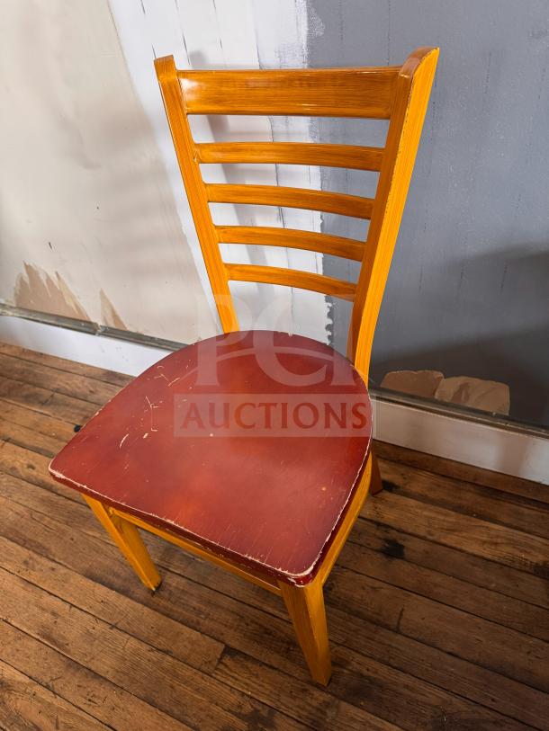 Vintage wooden dining chair with ladder back, red seat, visible wear, and scratches on the seat surface.