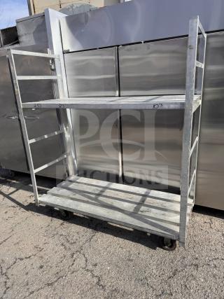 Heavy-duty aluminum stock cart with two shelves, sturdy construction. Markings on shelf edges indicate measurements. Industrial wheels for mobility.