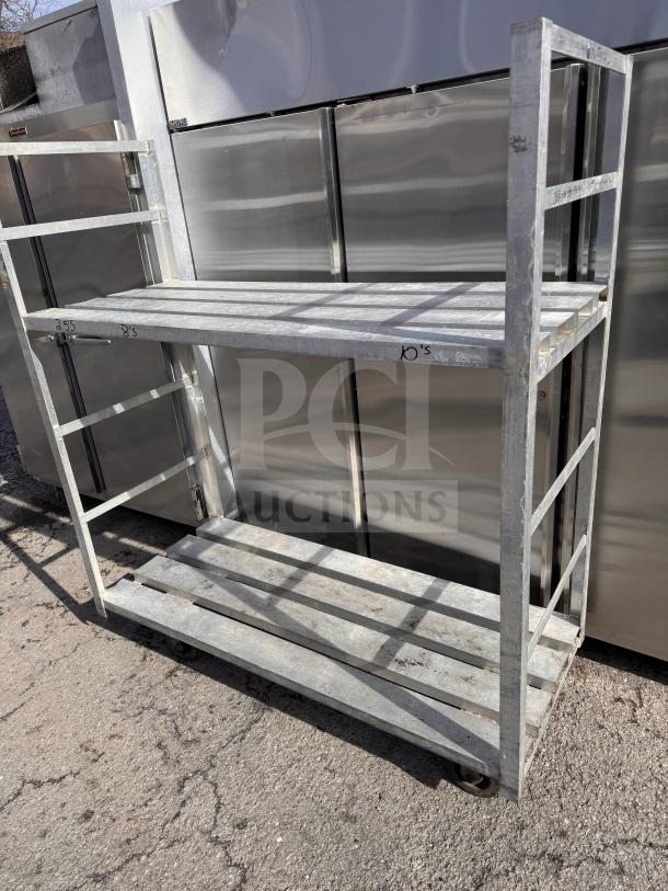 Heavy-duty aluminum stock cart, dual shelves, sturdy frame, caster wheels, visible wear, ideal for industrial use.