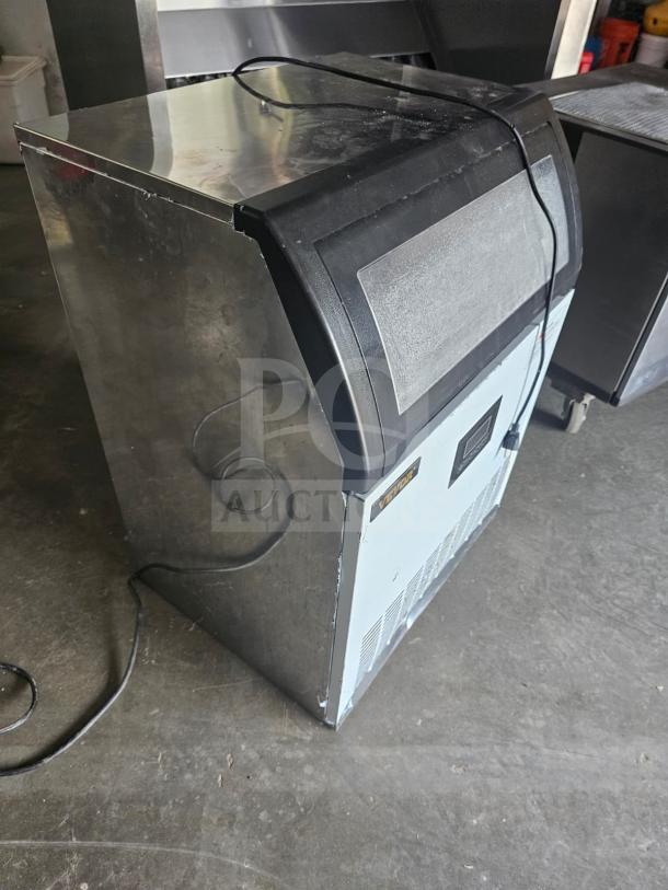 VEVOR SKF-E120F commercial ice maker, metallic finish, visible wear, lid slightly chipped, power cord attached, on concrete floor.