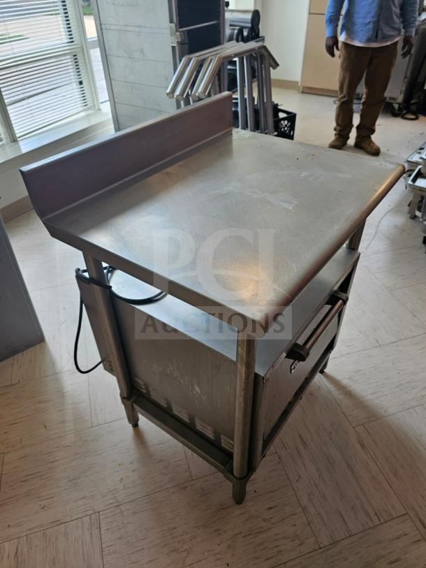 Stainless steel stand with raised back edge, sturdy design. Shows minor wear, ideal for kitchen or industrial use.