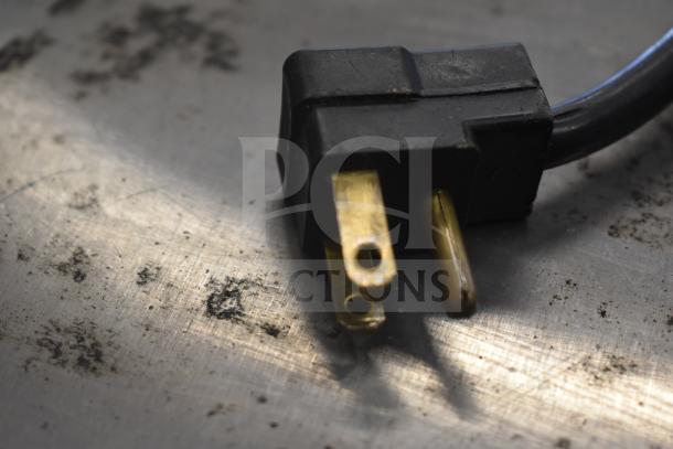 Close-up of a black power plug on a metal surface, connected to the Beverage Air SPED60HC-08C-2 refrigerated prep table.