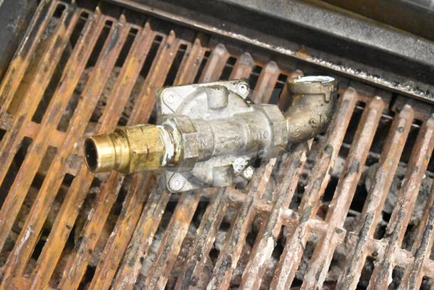 Commercial countertop gas-powered charbroiler grill with metal grates and visible wear, showing gas connection valve.