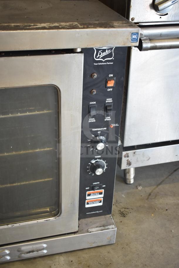 Duke stainless steel convection oven with view-through doors, thermostatic controls, and metal legs. Signs of wear visible.