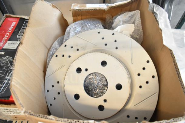 Cardboard box containing brake rotor, with drilled holes and bubble wrap, labeled for brake caliper. Box appears worn.