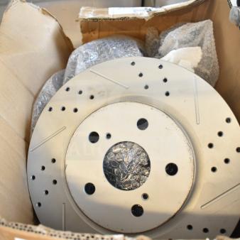 Cardboard box containing brake rotor, with drilled holes and bubble wrap, labeled for brake caliper. Box appears worn.