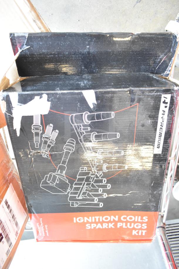 Ignition Coils Spark Plugs Kit in a scratched box with visible branding. Includes Door Lock Actuator, Brake Pad. Brand new.