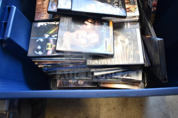 Two blue bins filled with various DVDs, including titles like "Flightplan" and "Gravity". Bins also include an LG DVD player.