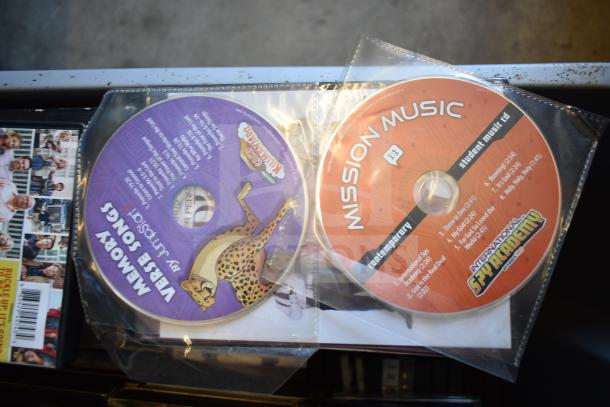 Lot of 2 bins containing DVDs, including "Mission Music" and "Memory Verse Songs" with visible labels, and wildlife print.