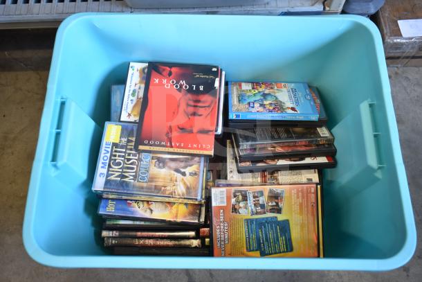A blue bin containing various DVDs including "Blood Work," "Night at the Museum" collection, and more, in used condition.
