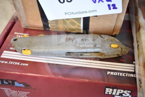 Lot of 12 items including a gray utility knife with yellow accents, set on a TST leather treatment box.