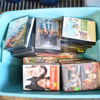 Lot of various DVDs in a large blue poly bin, featuring multiple genres and titles, some marked as rentals.