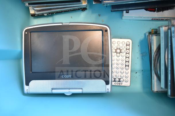 Coby portable DVD player with remote, alongside various DVDs in cases.
