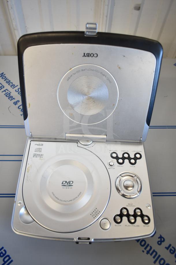 Portable Coby DVD player, open, showing controls and disc area. Signs of wear visible on surface. DVD Video and Dolby Digital labels.